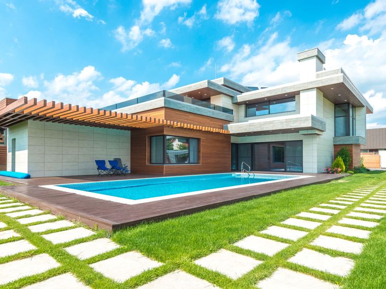 Pool mit umlaufender Terrasse an einem modernen Wohnhaus, daneben gepflasterter Rasen.