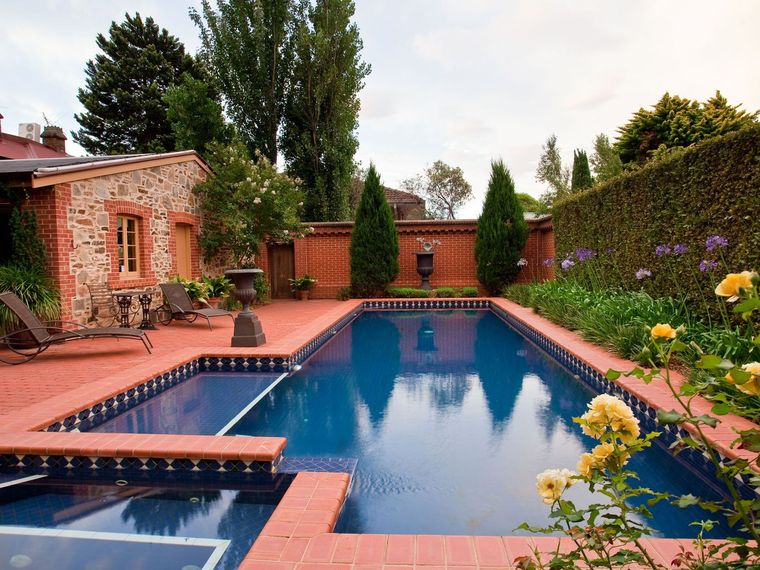 Gemauerter Pool mit dunkler Auskleidung in einem angelegten Garten mit Rosen und Hecke.