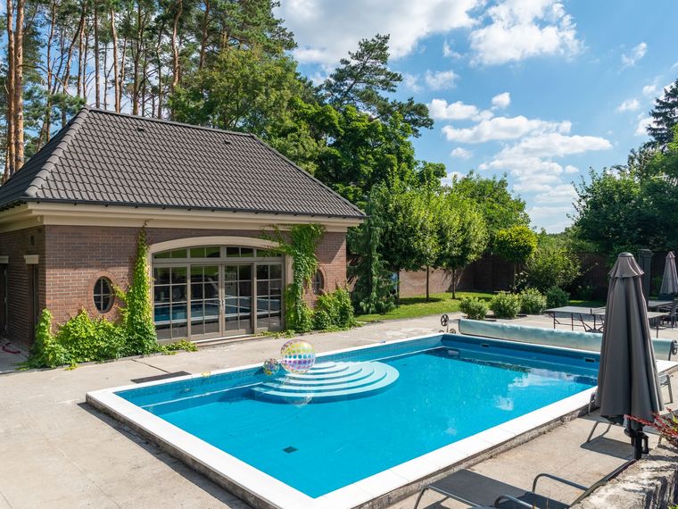 Rechteckiger Pool mit hellem Rand vor einem Poolhaus aus Backstein.